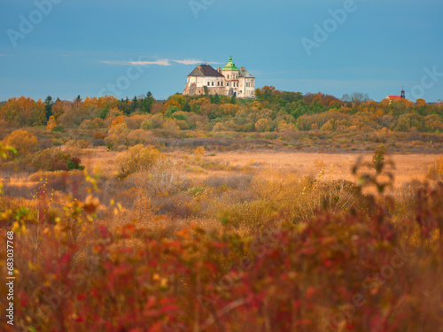 view to castle on hill through red bushes in autumn day under blue sky