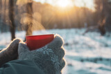 hot warming drink in a mug in hands with woolen gloves against the background of a winter frosty forest, picnic winter concept, cold snap