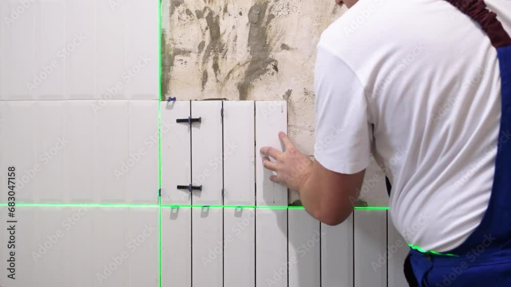 The hands of the tiler are laying white ceramic tile on the wall, using electronic laser level The hands of the tiler are laying white ceramic tile on the wall, using electronic laser level