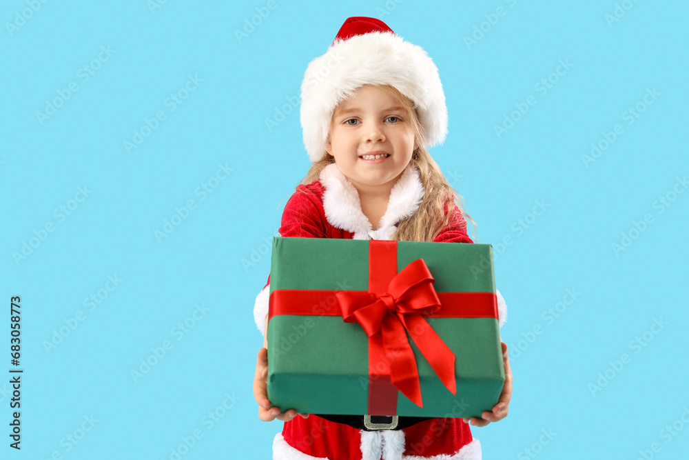 Cute little girl in Santa Claus costume with Christmas gift on blue background Cute little girl in Santa Claus costume with Christmas gift on blue background