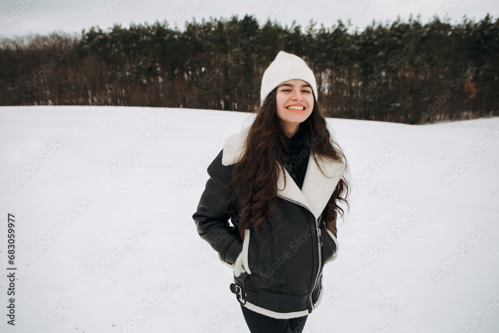 Young smiling woman posing in the field near forest in winter season snow on the ground, dressed warm leather jacket having fun, harsh conditions, wind blowing. Christmas Time, New Year
Young smiling woman posing in the field near forest in winter season snow on the ground, dressed warm leather jacket having fun, harsh conditions, wind blowing. Christmas Time, New Year