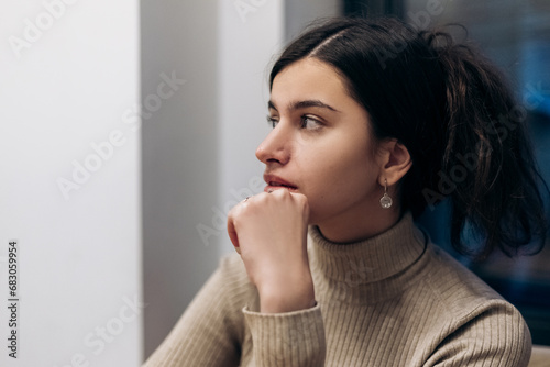 Young pretty confident woman sitting inside cafe waiting for order, thinking about something 