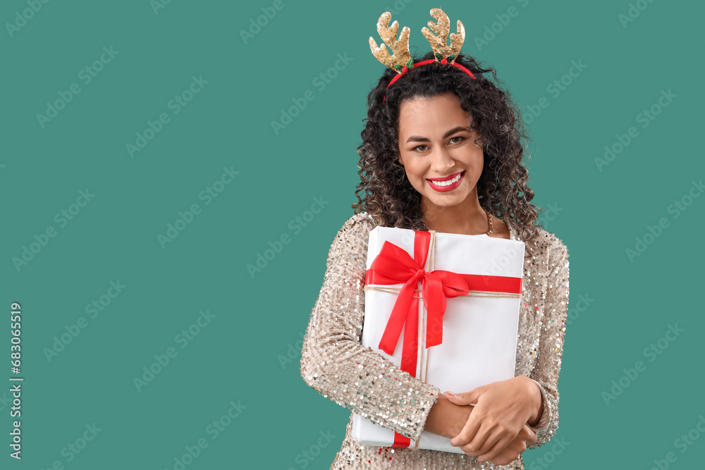 Beautiful African-American woman in reindeer horns with gift on green background. New Year celebration Beautiful African-American woman in reindeer horns with gift on green background. New Year celebration