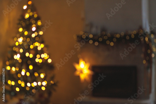 Christmas background golden bokeh. Atmospheric christmas eve at fireplace. Blurred image of illuminated christmas tree and festive decorated fireplace with lights in evening scandinavian room