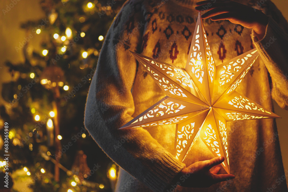 Φωτογραφία Merry Christmas! Stylish illuminated golden star in hands on background of modern decorated christmas tree with golden lights in evening room