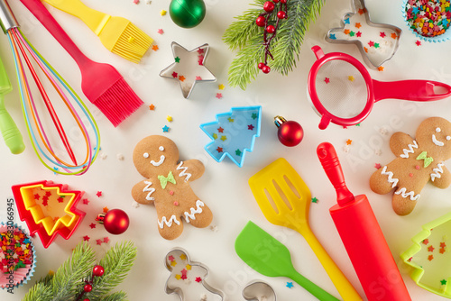 Сreating Christmas treats concept. Top view flat lay of gingerbread cookies, candies, baking gear, baking molds, fir branches, colorful stars on light beige background
