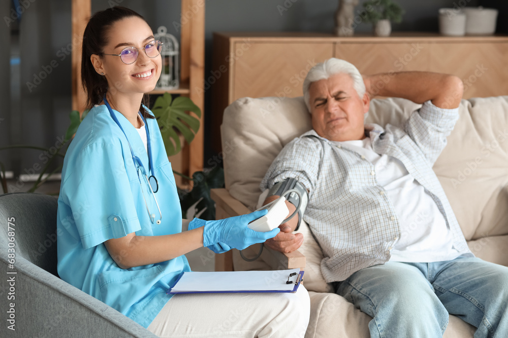 Fototapeta premium Female nurse measuring blood pressure of senior man at home