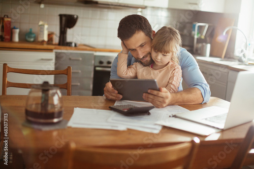 Father and daughter sitting at desk with documents using tablet at home © Geber86