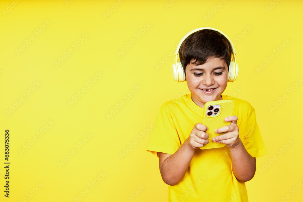 Cheerful child in vibrant yellow enjoying content on his phone with headphones, isolated on yellow. Cheerful child in vibrant yellow enjoying content on his phone with headphones, isolated on yellow.