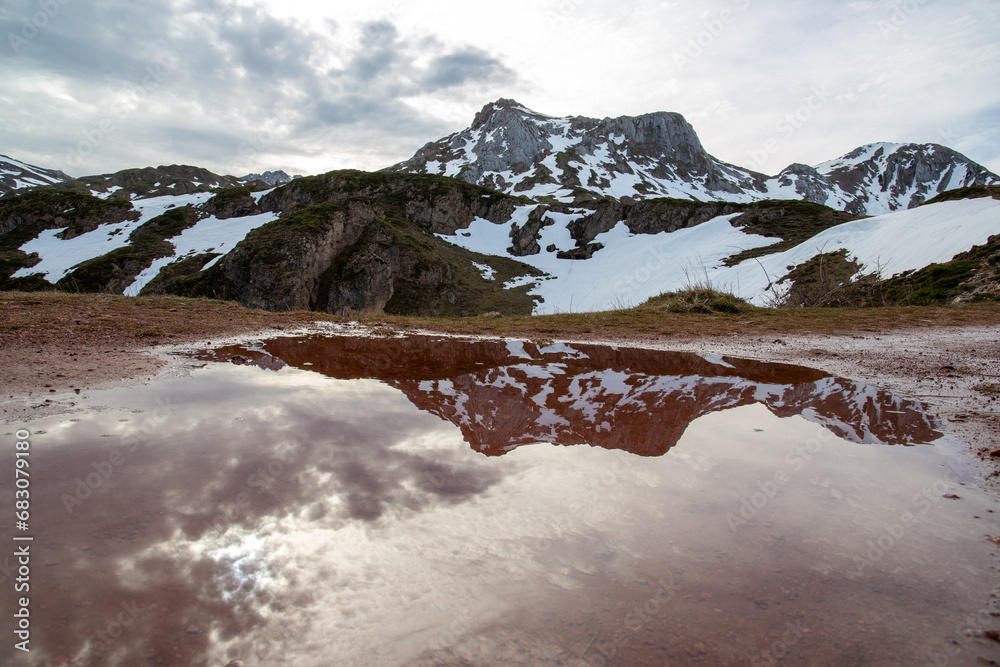 Snow-capped mountain reflected in a puddle. There are reddish tones due to a high iron content in the soil.