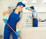 Cheerful girl from cleaning service washes floor in customer's house