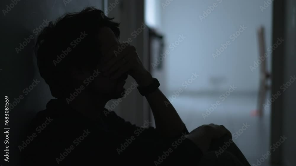 One depressed young man sitting on floor suffering from mental illness covering face with regret. Male person feeling anxious and depression