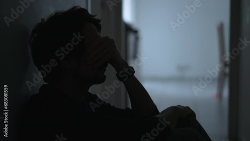 One depressed young man sitting on floor suffering from mental illness covering face with regret. Male person feeling anxious and depression photo