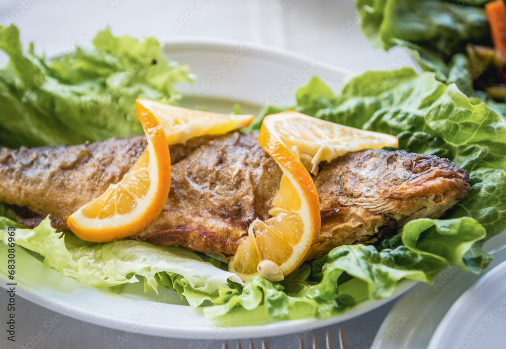 Georgian food in restaurant - roasted fish with lemon slices Georgian food in restaurant - roasted fish with lemon slices