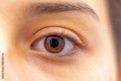 macrophotograph of a brown human eye of a young female with traces of black mascara on the eyelashes and surrounding skin area. #683093773