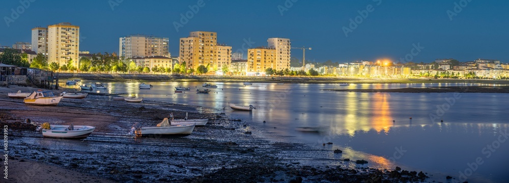 panoramic view of the riverside area of the city of Barreiro with residential buildings, low tide with small fishing boats. Night image.