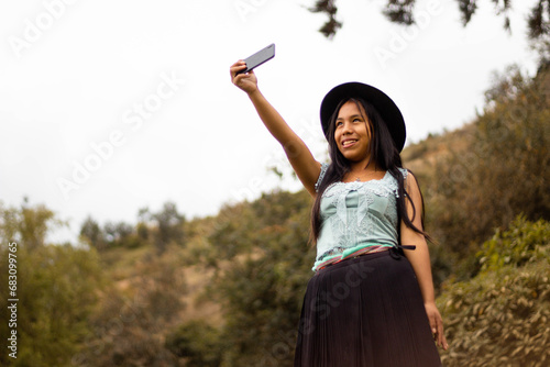 Foto de una feliz y bonita campesina caucásica con un sombrero hablando por un teléfono celular en los Andes peruanos. Mujer usando teléfono móvil photo