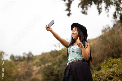 Foto de una feliz y bonita campesina caucásica con un sombrero hablando por un teléfono celular en los Andes peruanos. Mujer usando teléfono móvil