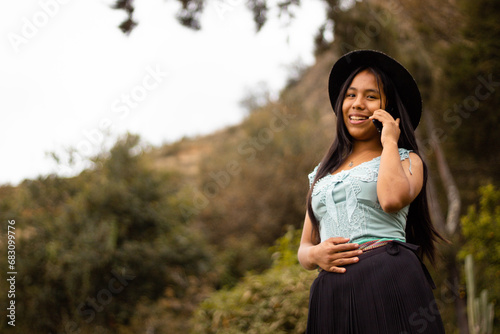 Foto de una feliz y bonita campesina caucásica con un sombrero hablando por un teléfono celular en los Andes peruanos. Mujer usando teléfono móvil