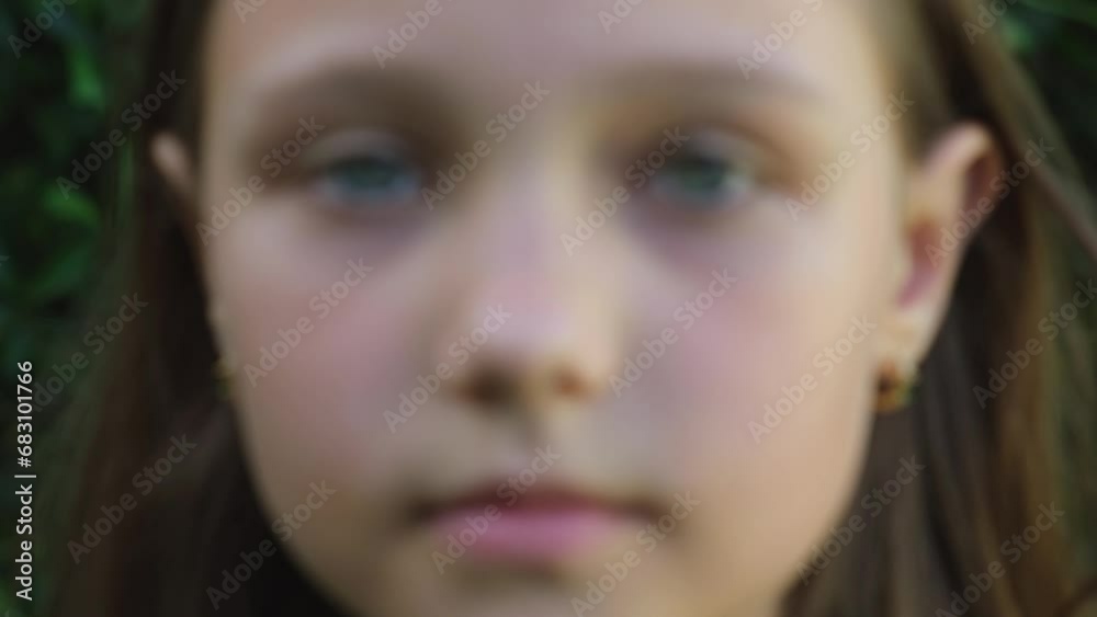 Portrait of a little beautiful girl looking at the camera, standing on the street in the city on a summer day. Young sad thinking curious child looking at camera closeup outdoors. Face Eyes Serious Portrait of a little beautiful girl looking at the camera, standing on the street in the city on a summer day. Young sad thinking curious child looking at camera closeup outdoors. Face Eyes Serious