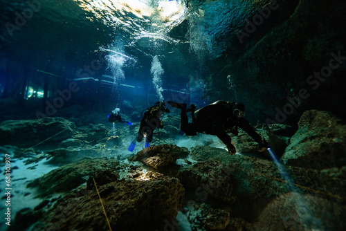 Anonymous Scuba divers with fins, scuba gears and flashlights swimming through the caverns of Cenote Dos Ojos, Mexico photo
