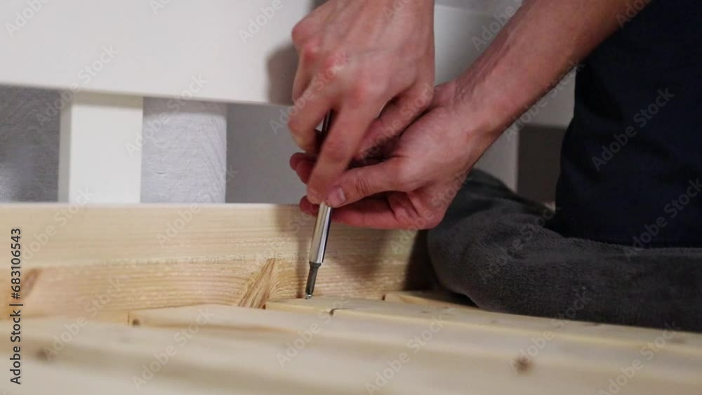 A young man manually tightens a screw with a screwdriver. A young man manually tightens a screw with a screwdriver.