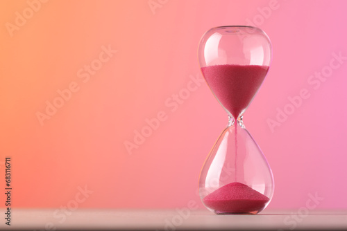 Hourglass with flowing pink sand on table against color background. Space for text