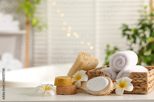 Composition with different spa products and plumeria flowers on white table in bathroom. Space for text