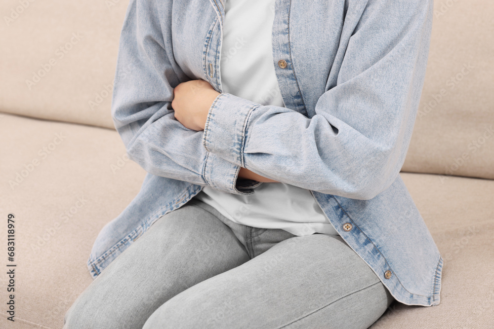 Young woman suffering from stomach pain on sofa, closeup Young woman suffering from stomach pain on sofa, closeup