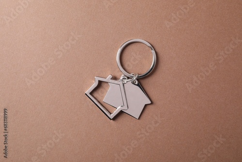 Metallic keychains in shape of houses on light brown background, top view