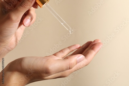 Woman applying cosmetic serum onto her finger on beige background, closeup