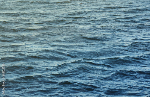 The raging waters of the river. Top view background texture of the raging elements. White foam on blue waving water in evening.