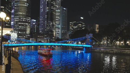 a night shot of a boat passing under the historic cavanagh bridge and the singapore river in singapore photo