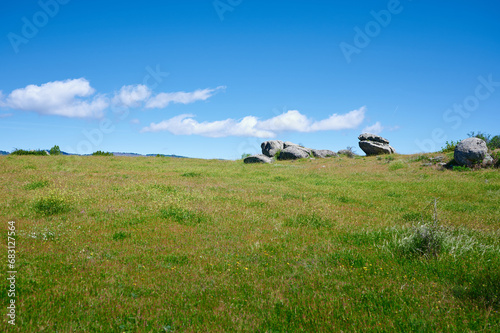 Large granite rocks dot a meadow, completely green when spring arrives. Rural landscape of Madrid with blue sky at the background.