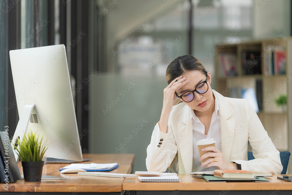 An Asian businesswoman working on a desktop computer is stressed has a headache, and thinks hard from work at the office. An Asian businesswoman working on a desktop computer is stressed has a headache, and thinks hard from work at the office.