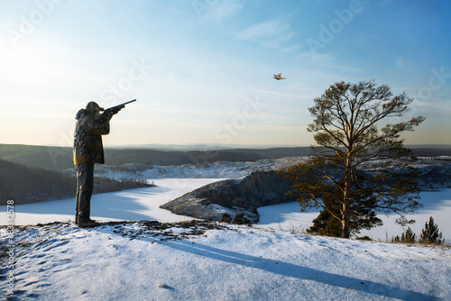 hunter shooting to the flying pheasant at winter period. hunter man shooting with his automatic shotgun photo