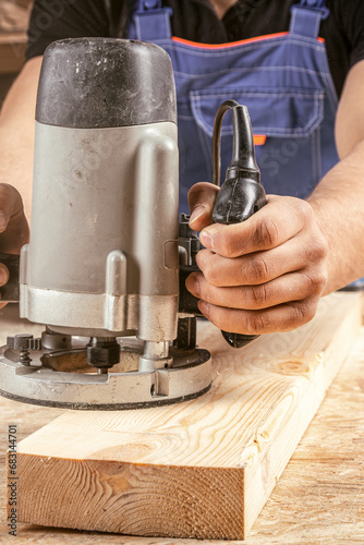 Male carpenter using electric sander to polish wooden plank in joinery workshop