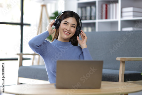 Young Asian woman wearing headphones listening to music in the living room at home.