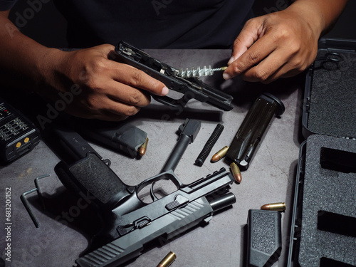 Gunsmith cleaning pistol Assemble, dismantle, and maintain with a brush to clean a black 9 mm pistol on an old cement floor pattern table. Gun maintenance gear.