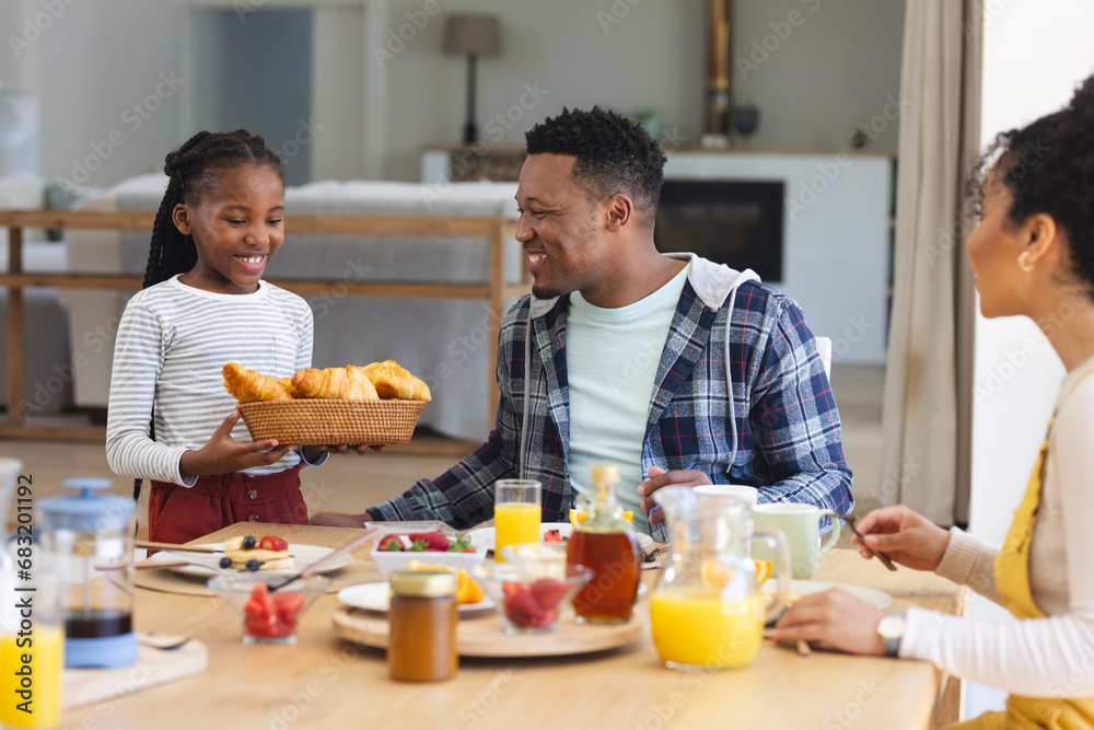 Happy african american girl bringing basket of croissants at table at home, copy space