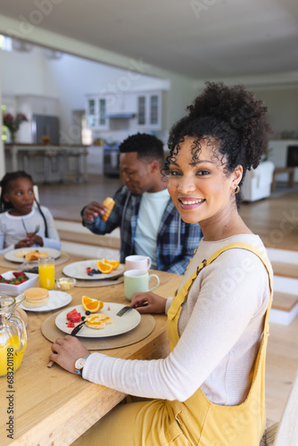 Happy african american woman sitting at table, having a snack with family at home, copy space