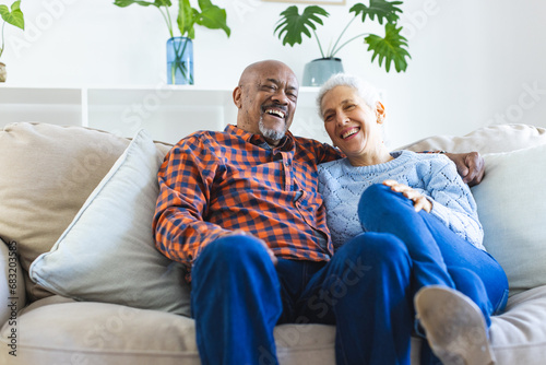 Happy diverse senior couple sitting on sofa and embracing in sunny living room photo