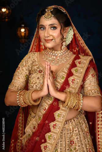 Stunning Indian bride dressed in traditional bridal lehenga with heavy gold jewellery and veil, standing with her hands in a namaste gesture