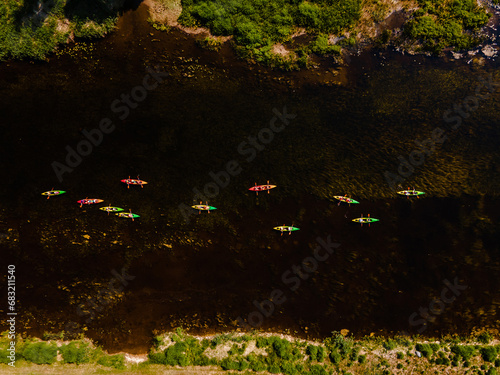 Aerial shot of colorful kayaks gliding over a dark river with vivid underwater vegetation