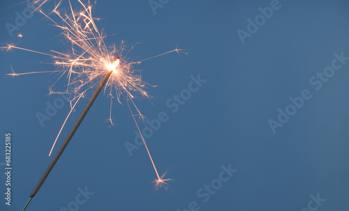 One sparkler burning on blue background, space for text.
