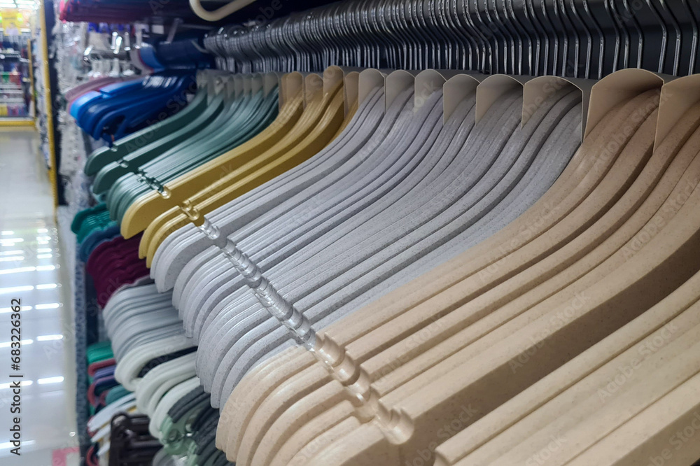 A row of clothes hangers in a clothing store. The hangers are made of plastic, are white, yellow, and green in color, and have a rotating metal hook and notches for straps A row of clothes hangers in a clothing store. The hangers are made of plastic, are white, yellow, and green in color, and have a rotating metal hook and notches for straps