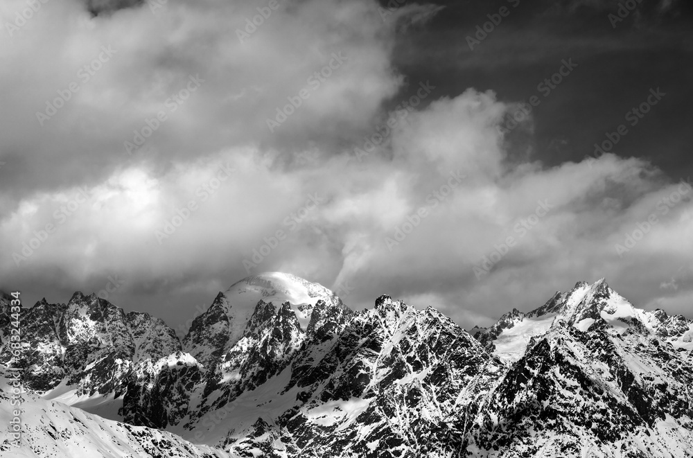 Black and white view on snow mountaims in clouds at sun winter day