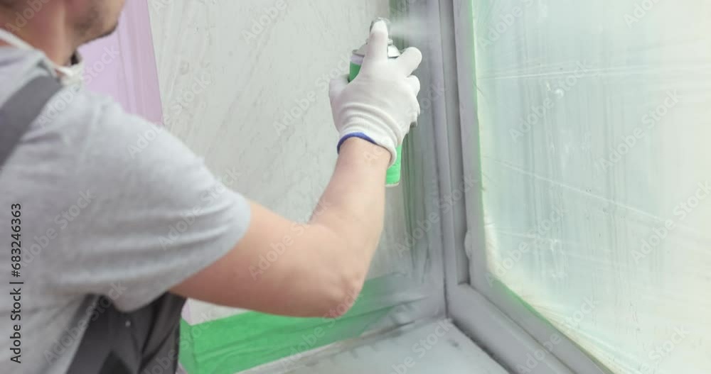 Builder paints a window layer with white spray paint. Features of painting door and window slopes