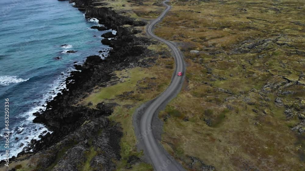 Aerial of a red car driving on a bendy road at the coastline of Iceland Aerial of a red car driving on a bendy road at the coastline of Iceland