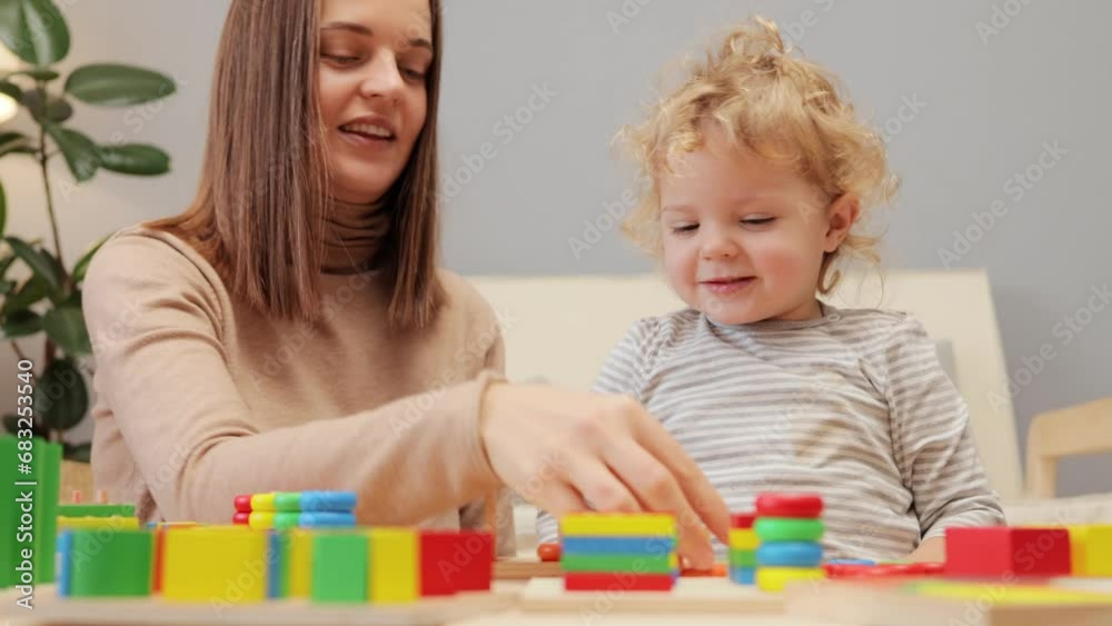 Child development. Educational toys. Communication and creativity. Emotional and social development. Positive Caucasian woman playing with her infant baby daughter in home interior. Child development. Educational toys. Communication and creativity. Emotional and social development. Positive Caucasian woman playing with her infant baby daughter in home interior.